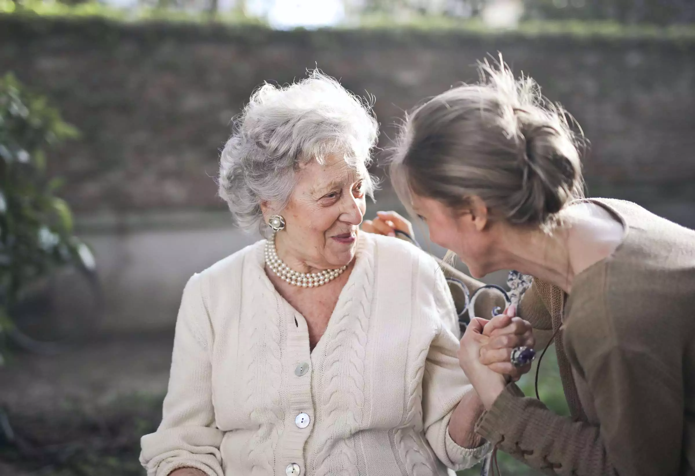 An elderly woman and a caregiver enjoying conversation outdoors.
