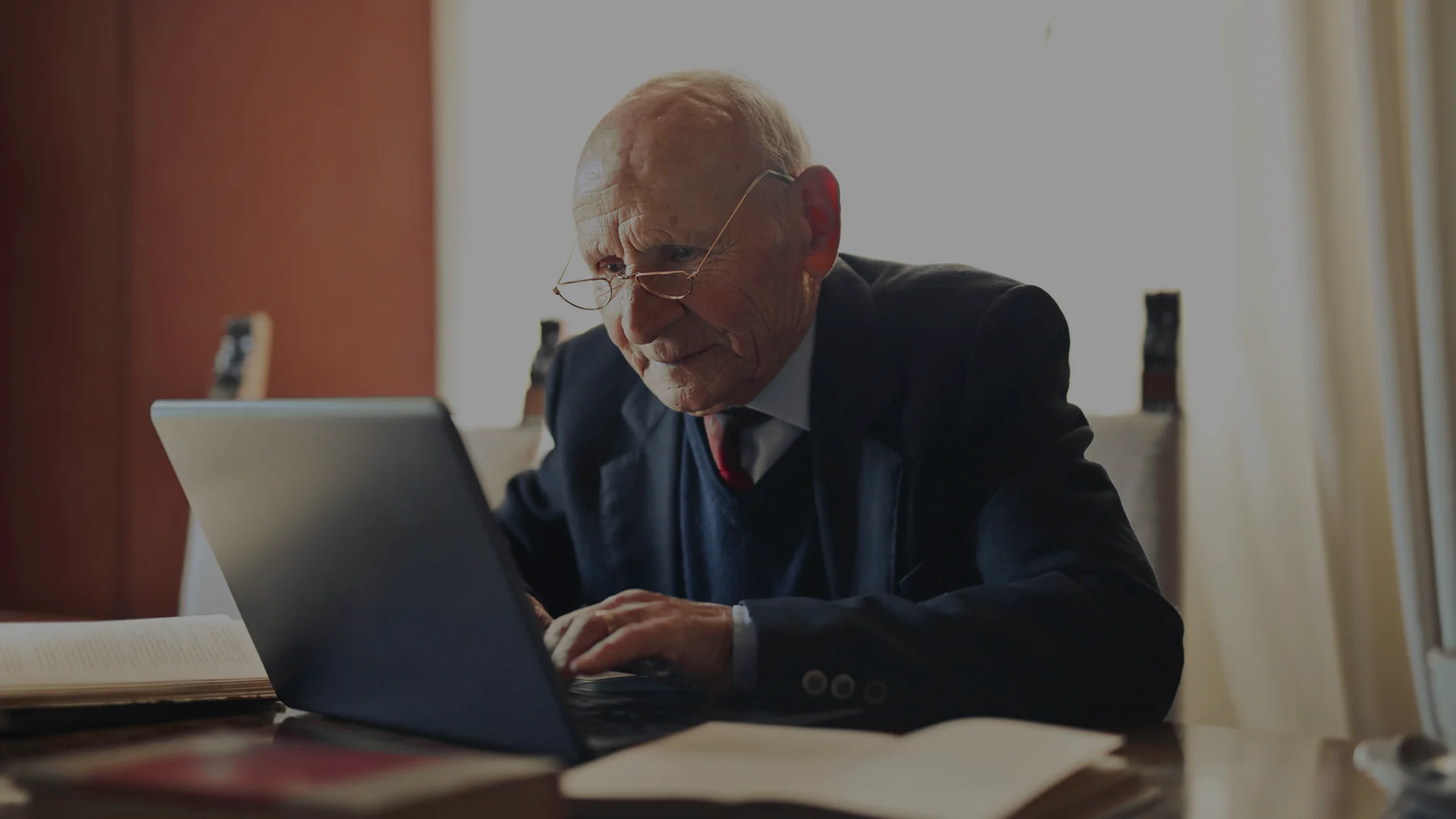 Elderly man using a laptop at a table.