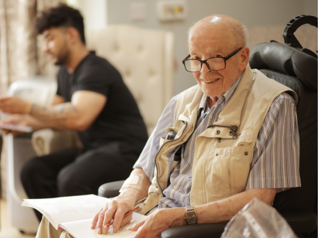 Elderly man reading in care home setting.