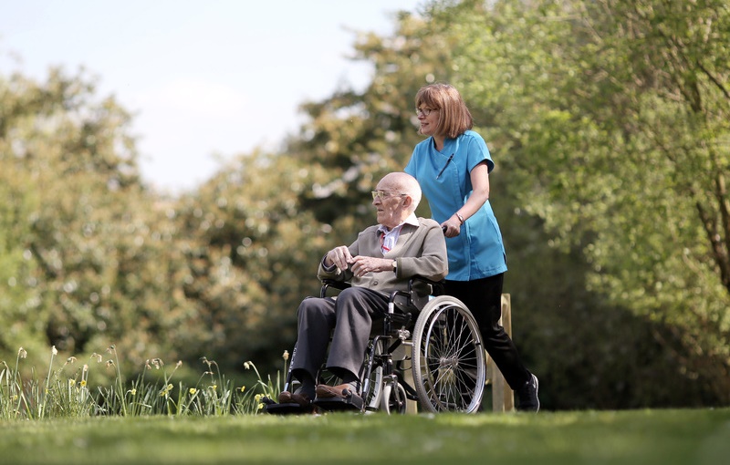 A caregiver assisting a resident in a wheelchair outdoors.