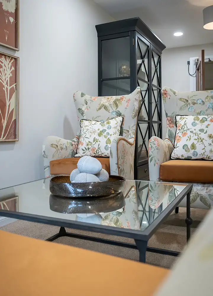 Cozy common area with floral armchairs and a glass table.