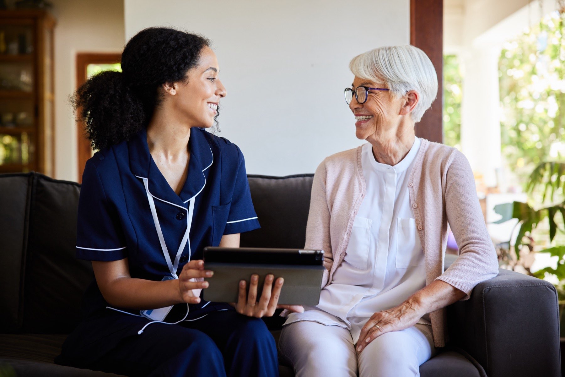 A caregiver and resident share a joyful moment on a couch.