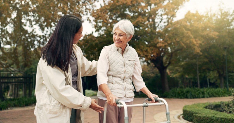 A caregiver assisting an elderly woman outdoors.