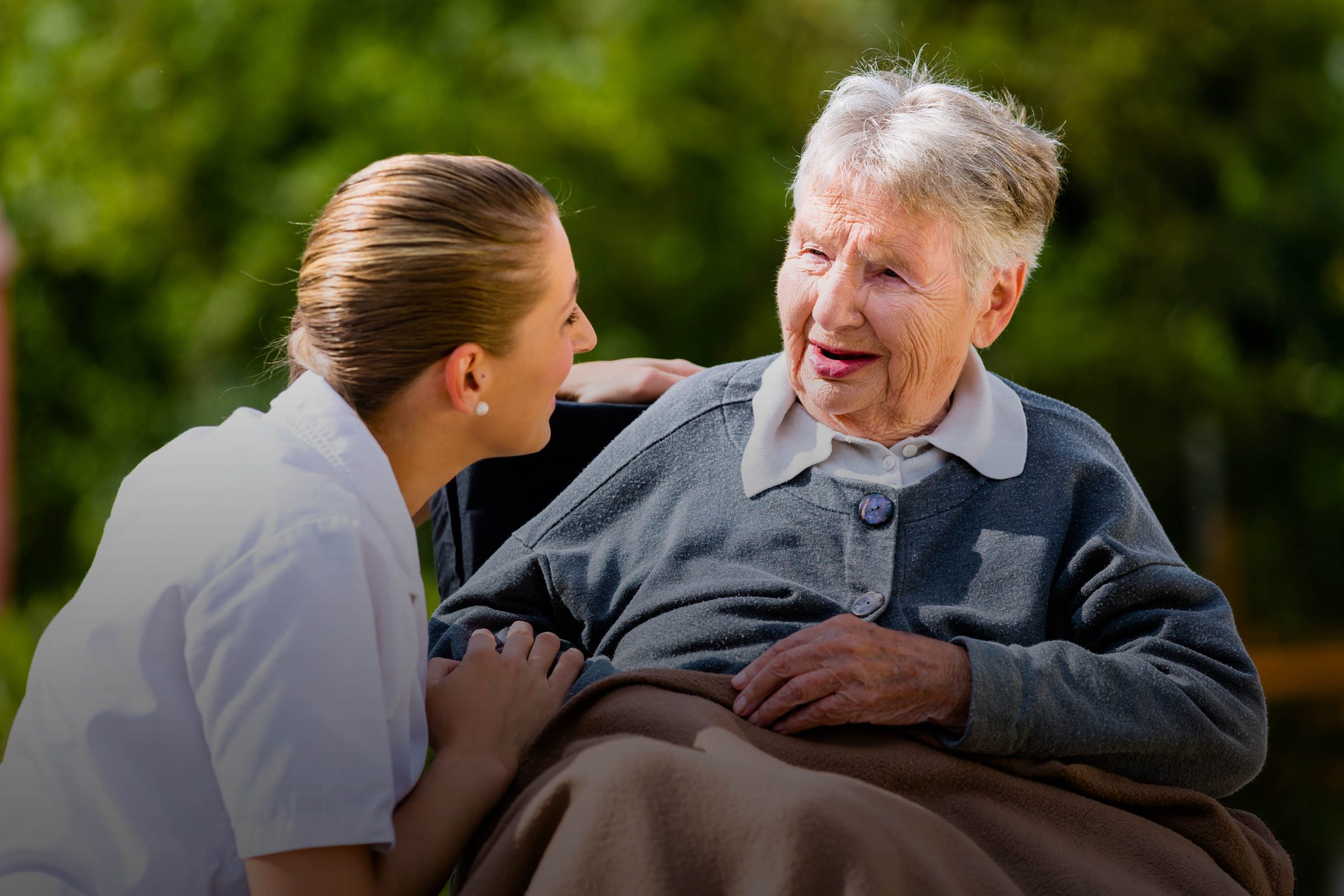 Healthcare worker interacting with a senior resident outdoors.
