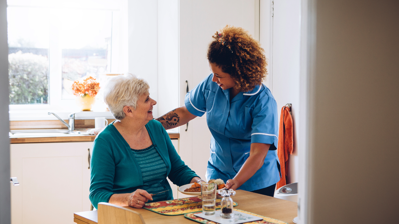 Caregiver serves food to a senior resident in a dining setting.