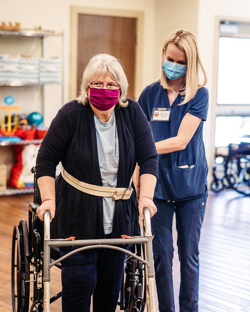 A caregiver assists a resident using a walker.