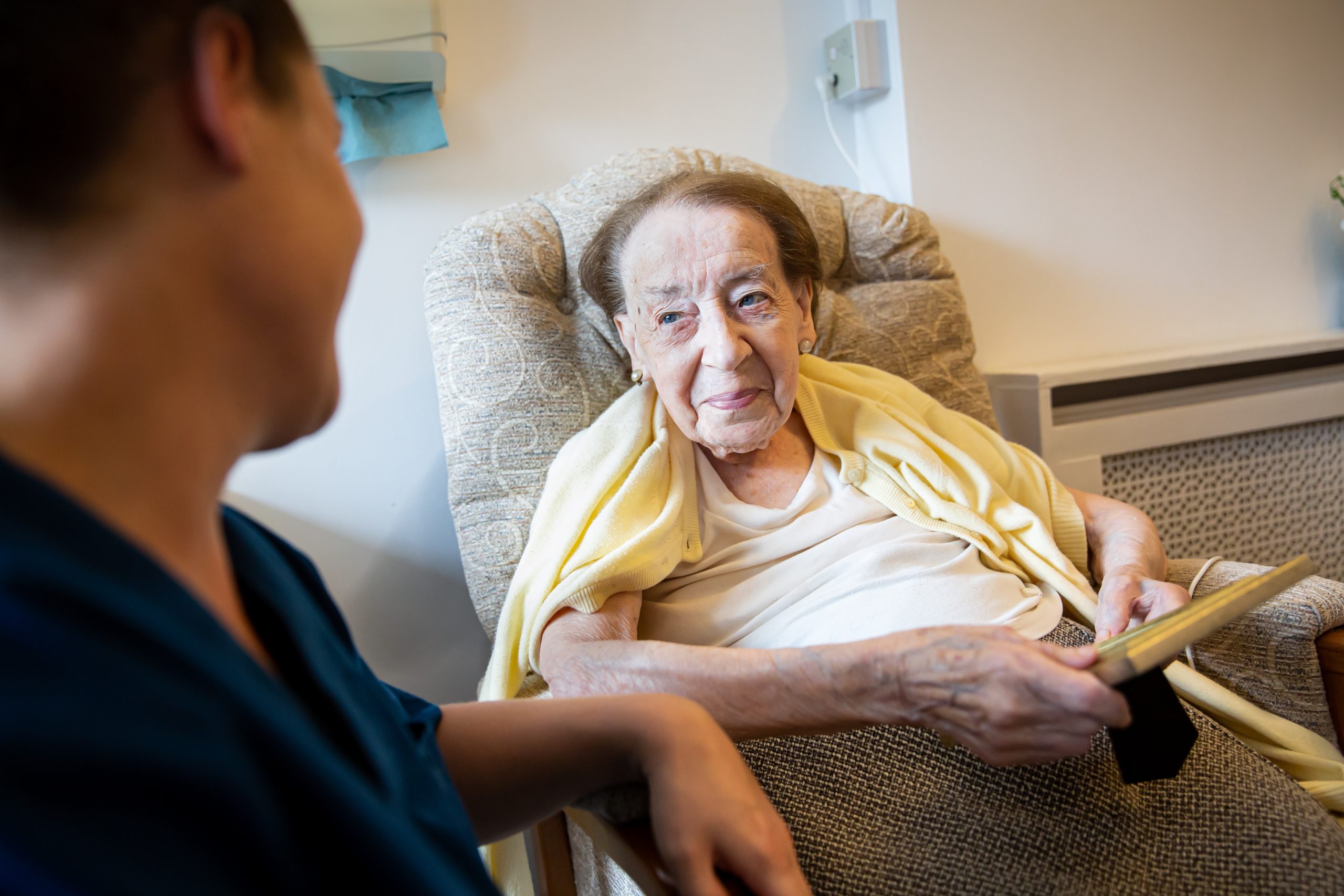 An elderly woman smiling with a staff member nearby.
