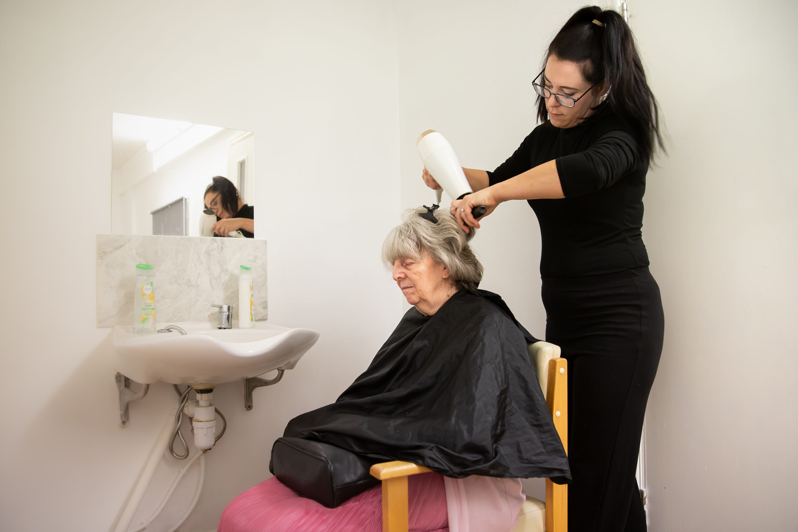Hair stylist assisting a resident in a salon setting.