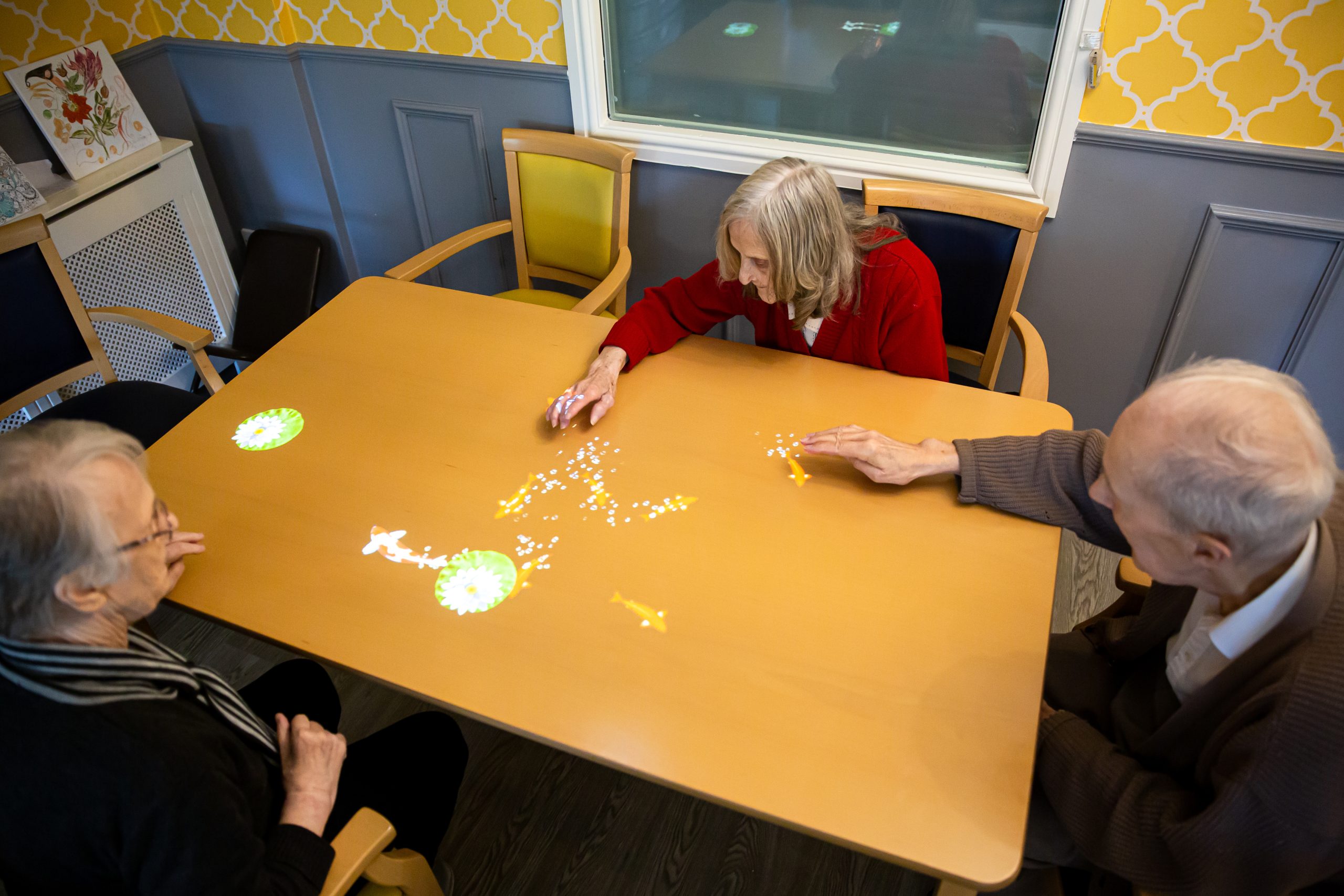 Three seniors engaging with interactive projection on a table.