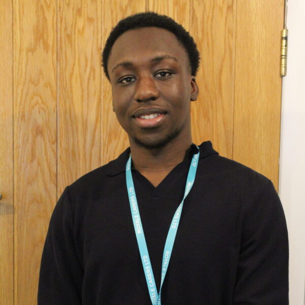 Staff member wearing a name badge in front of wood paneling.