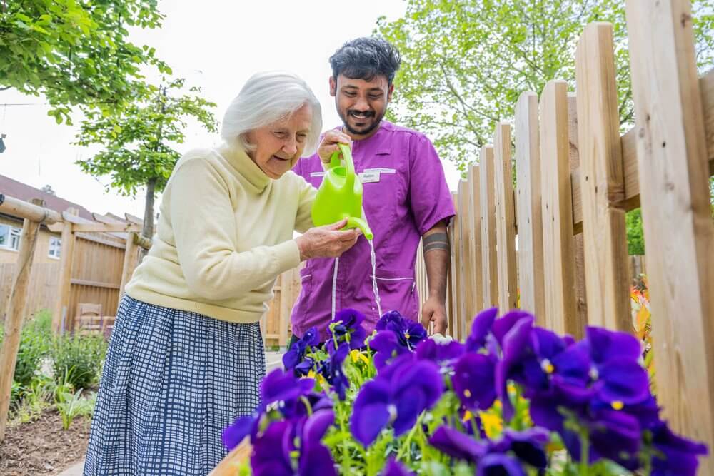 Elderly woman watering flowers with staff support