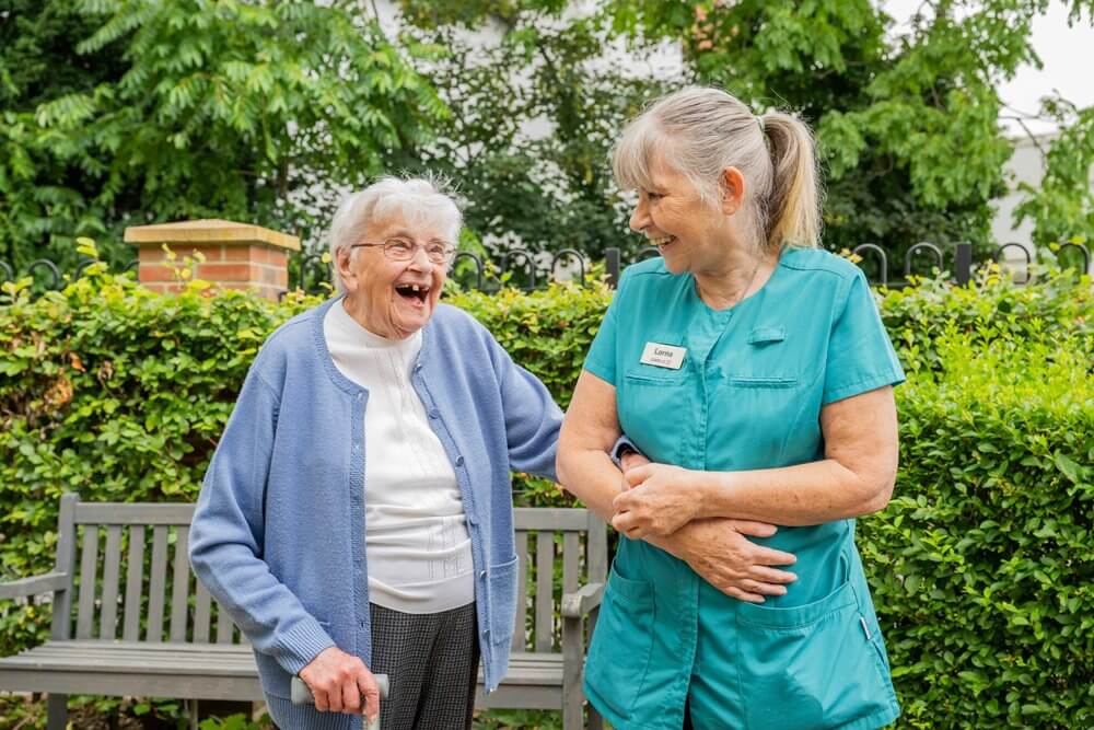 Senior resident laughing with staff outdoors