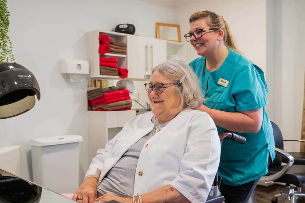 A staff member assists a resident at a beauty station.