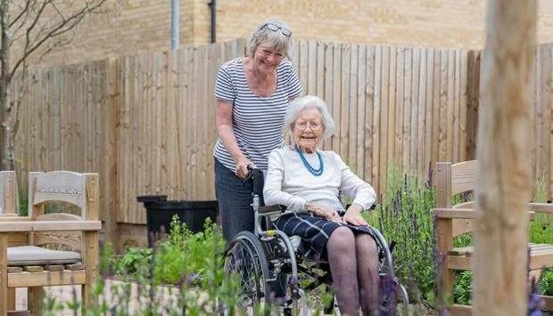 Caregiver assisting an elderly woman in a garden.