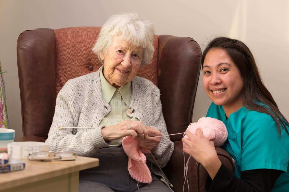 Elderly woman knitting with a caregiver.