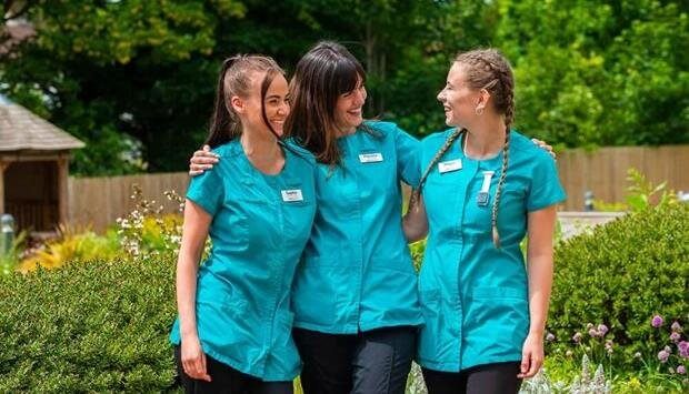 Three staff members in turquoise uniforms outdoors.