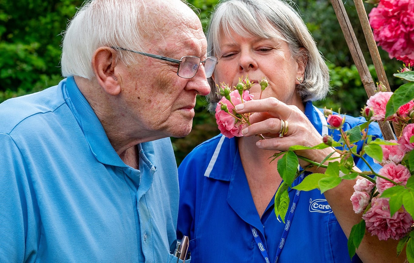 Resident and staff member enjoying flowers outdoors.