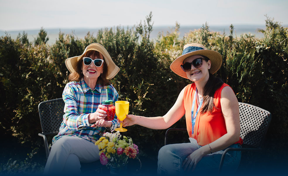 Two women enjoying drinks outdoors in a garden setting.