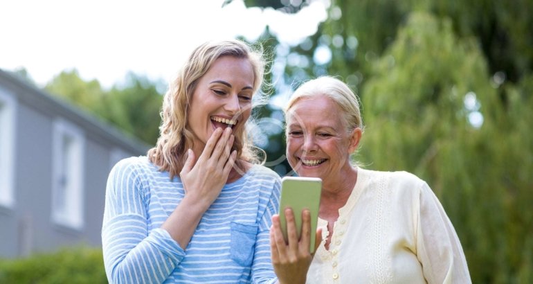 Two women smiling at a phone outdoors
