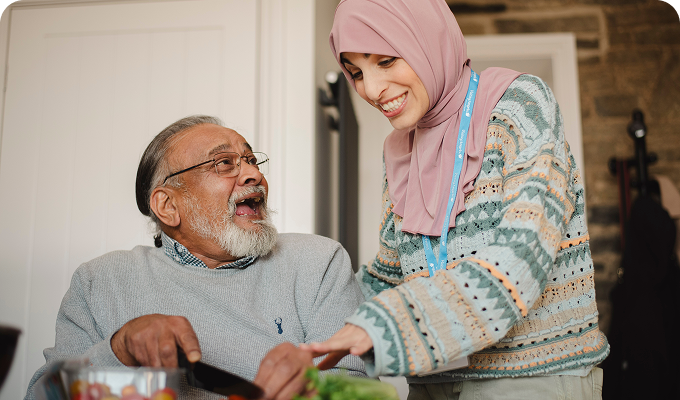 Senior and caregiver interacting while preparing food.