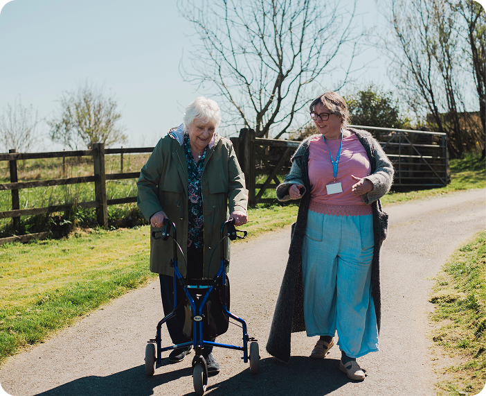 Staff assisting resident outdoors with a walker.