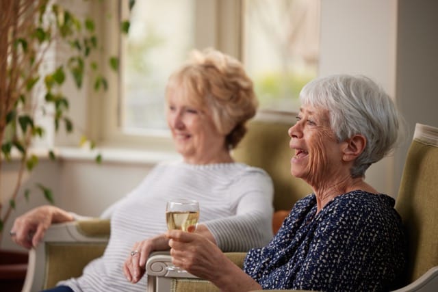 Two elderly women enjoying drinks and company indoors.
