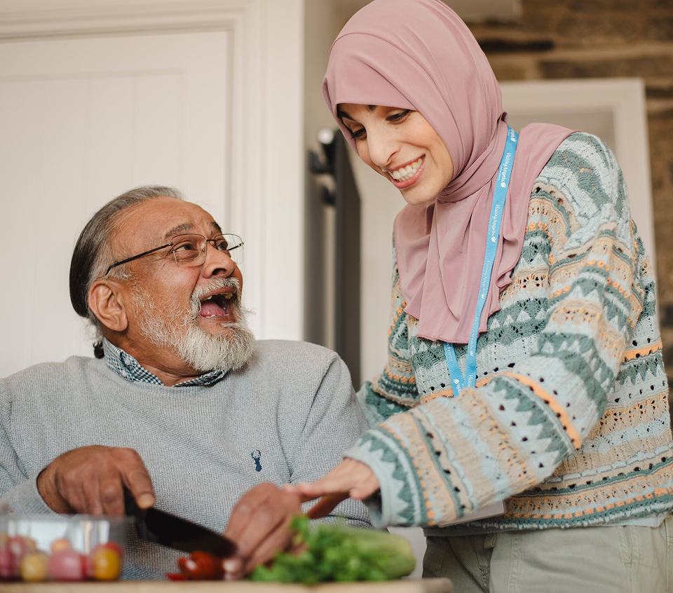 A caregiver preparing food with an elderly man indoors.