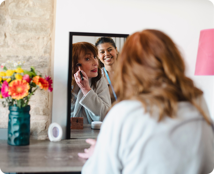 A senior woman applying makeup with staff assistance.