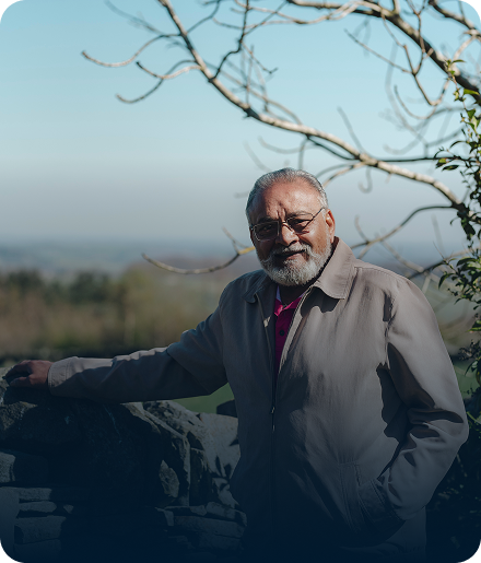 Elderly man standing in a scenic outdoor area.
