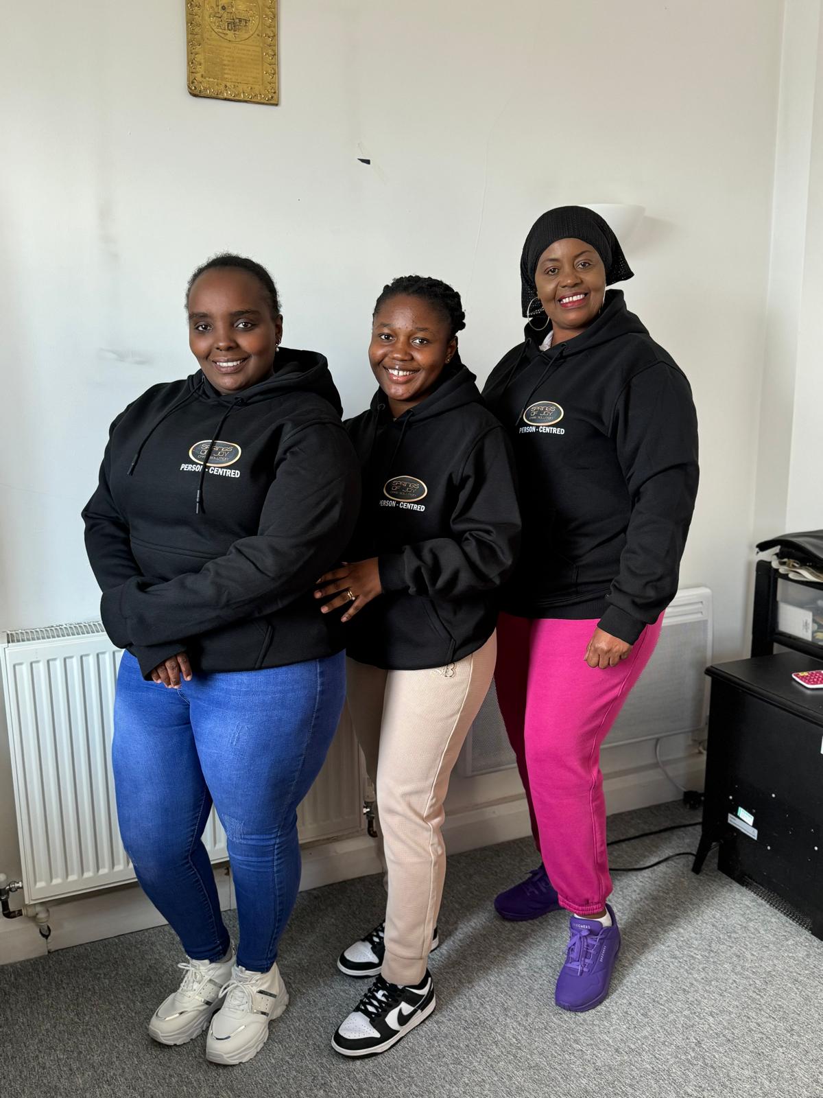 Three staff members in branded hoodies smiling together.
