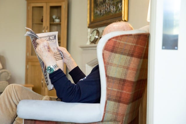 Resident reading a newspaper in a cozy chair.