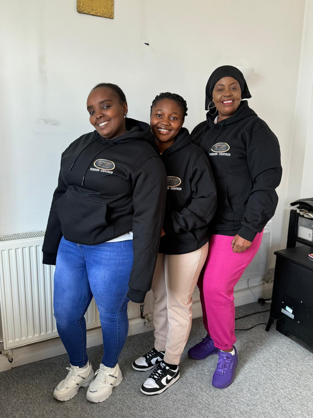 Three staff members wearing hoodies and smiling