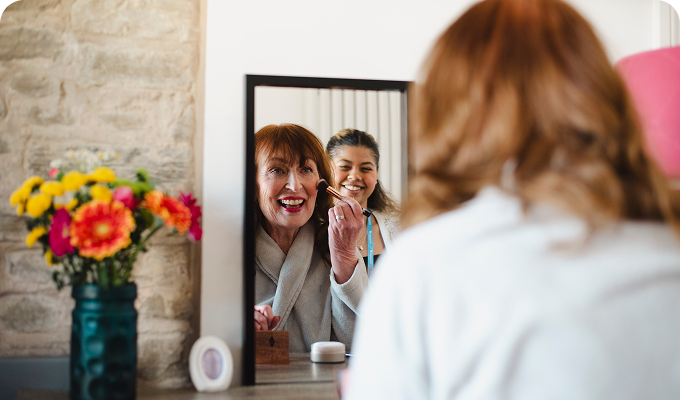 Woman applying makeup with caregiver assistance