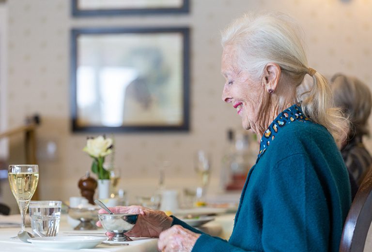 Elderly woman enjoying a meal in a dining setting.