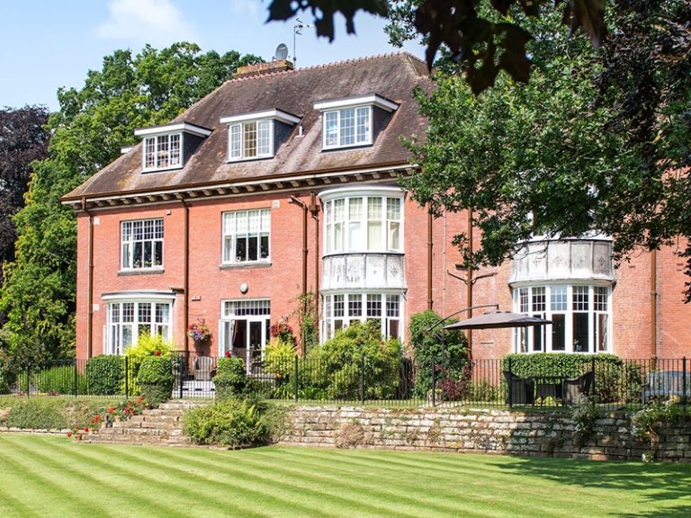 Exterior view of a care home building surrounded by gardens.
