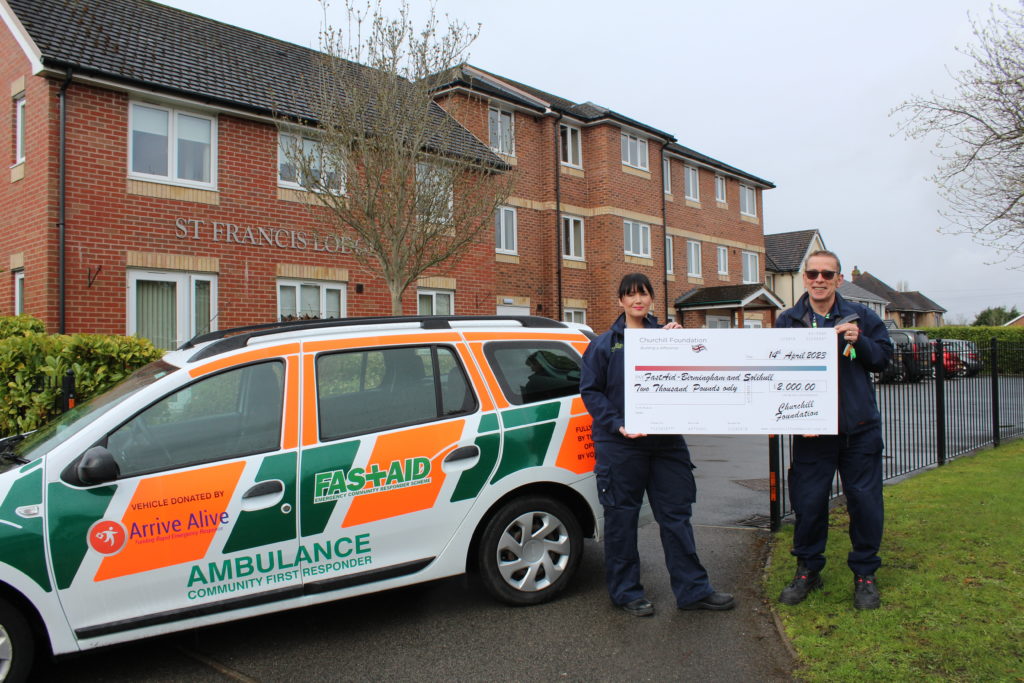 Two responders with a large check outside a facility