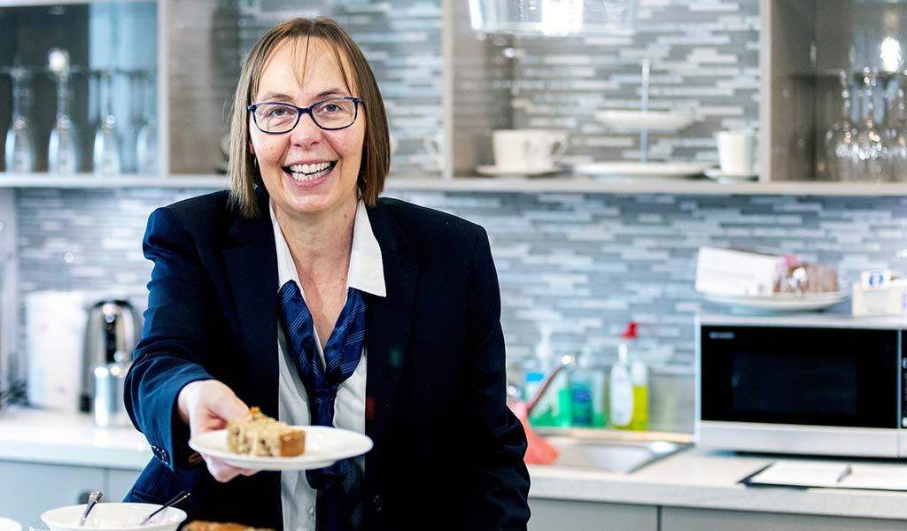 Staff member serving food in a facility kitchen.