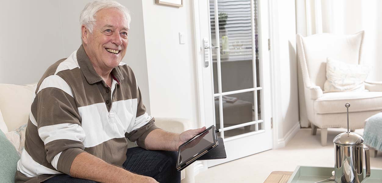 A senior man smiling while using a tablet.