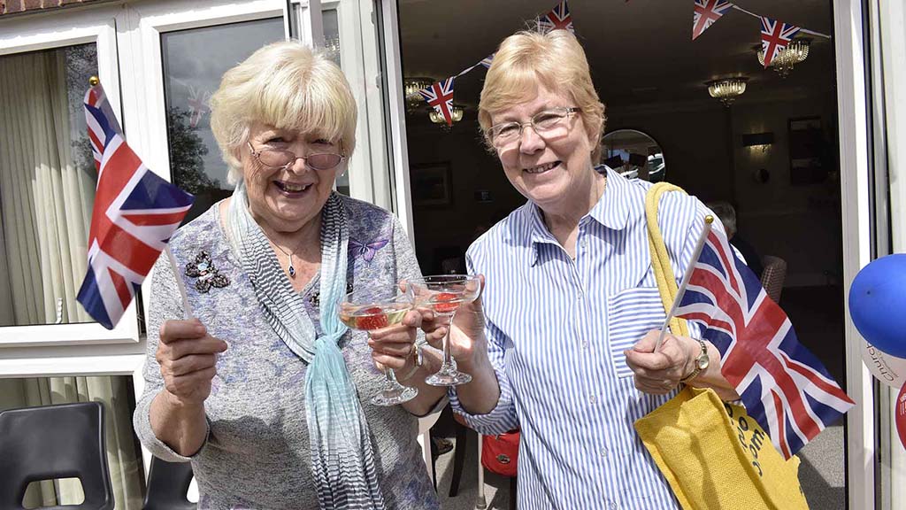 Two women celebrating with flags and drinks.