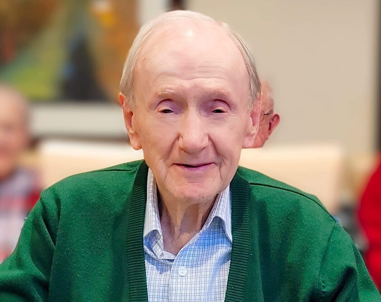 Smiling resident in a common area with staff in background