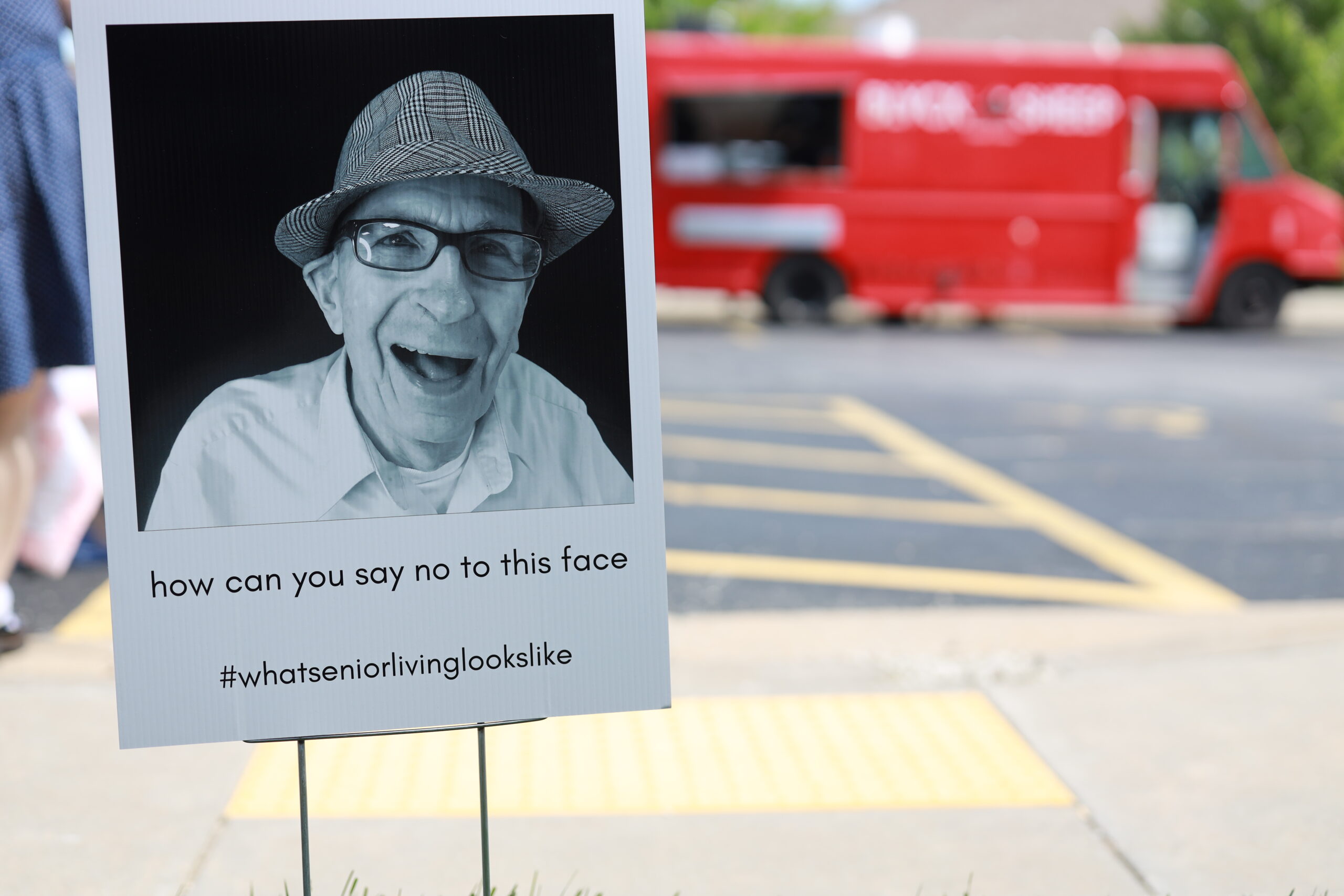A sign featuring a smiling resident with a red vehicle in the background