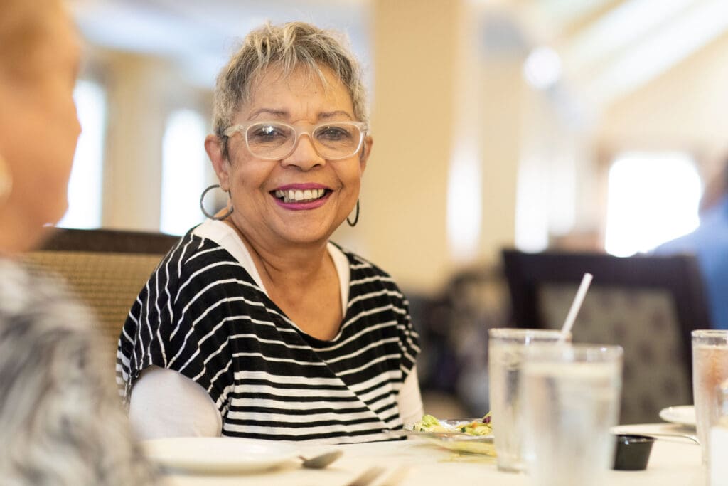 Resident enjoying a meal with a smile in the dining room