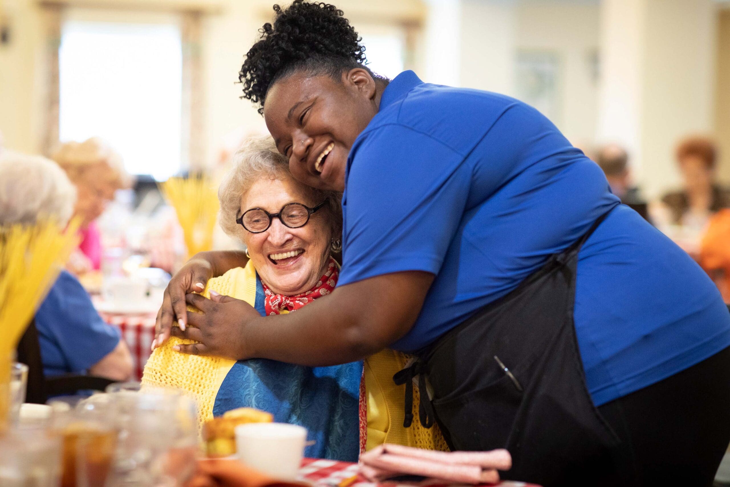 Staff member hugging a smiling resident in a dining area