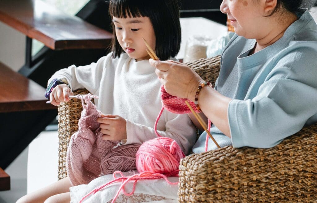 An older woman and young girl knitting together in a cozy indoor space