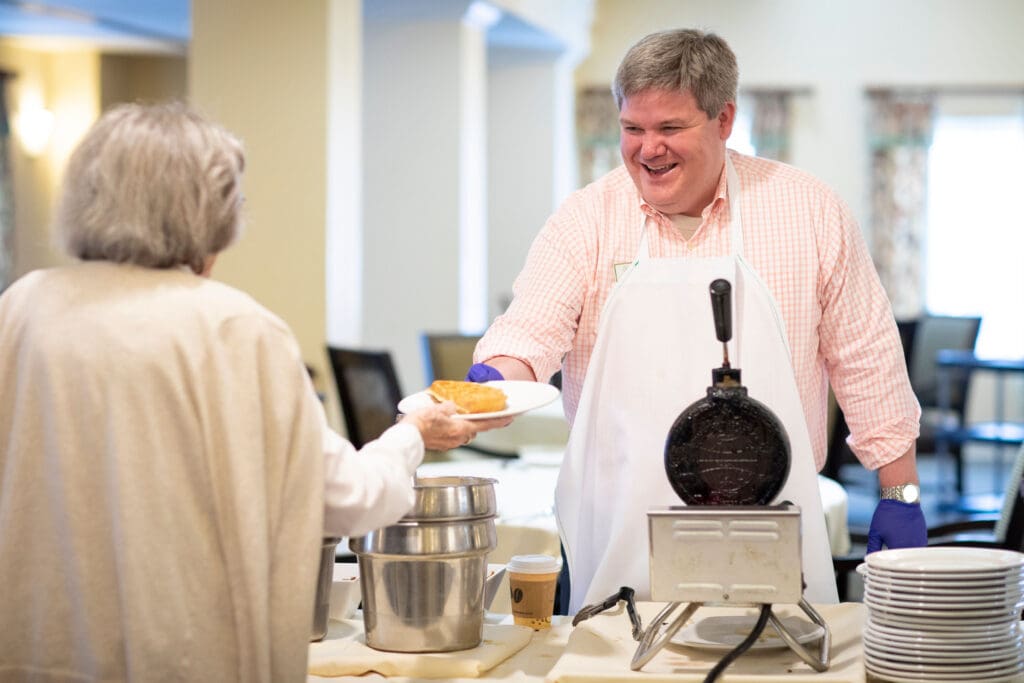Staff serving food to a resident in a bright dining area