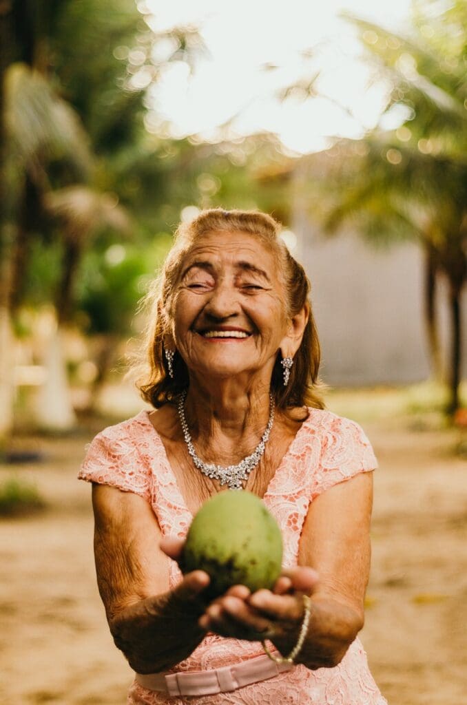Senior woman smiling while holding a green fruit outdoors