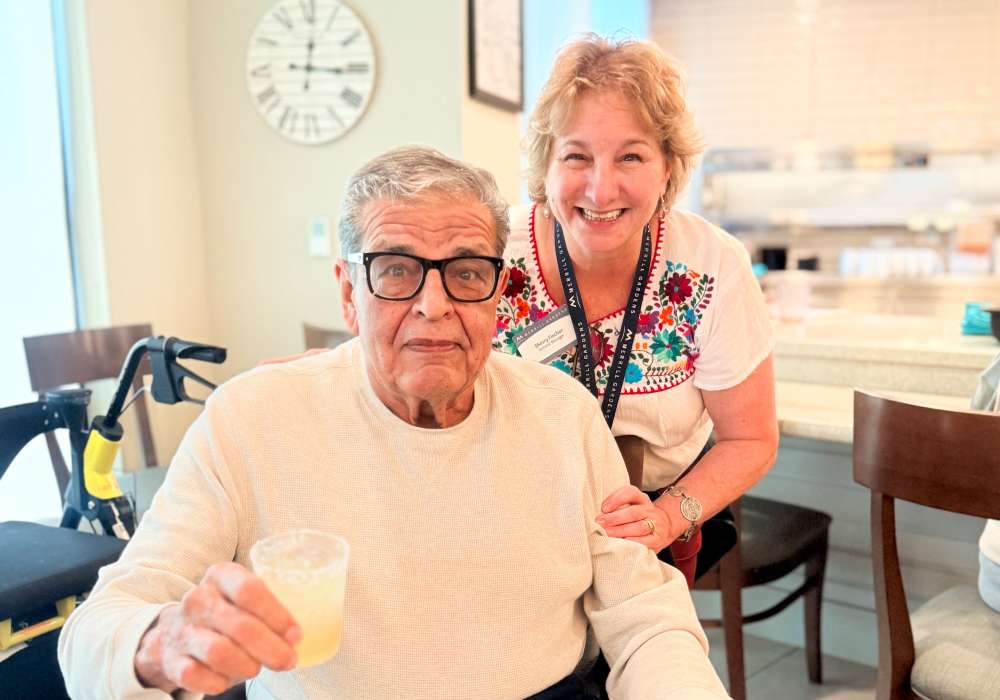 An elderly man smiles with a staff member in a common area