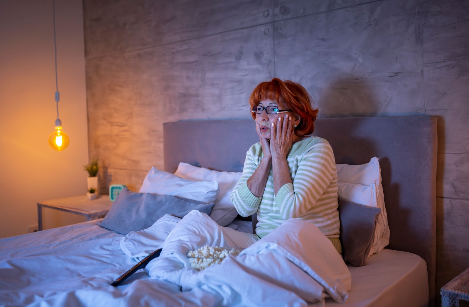 Elderly woman watching a movie in bed, looking surprised