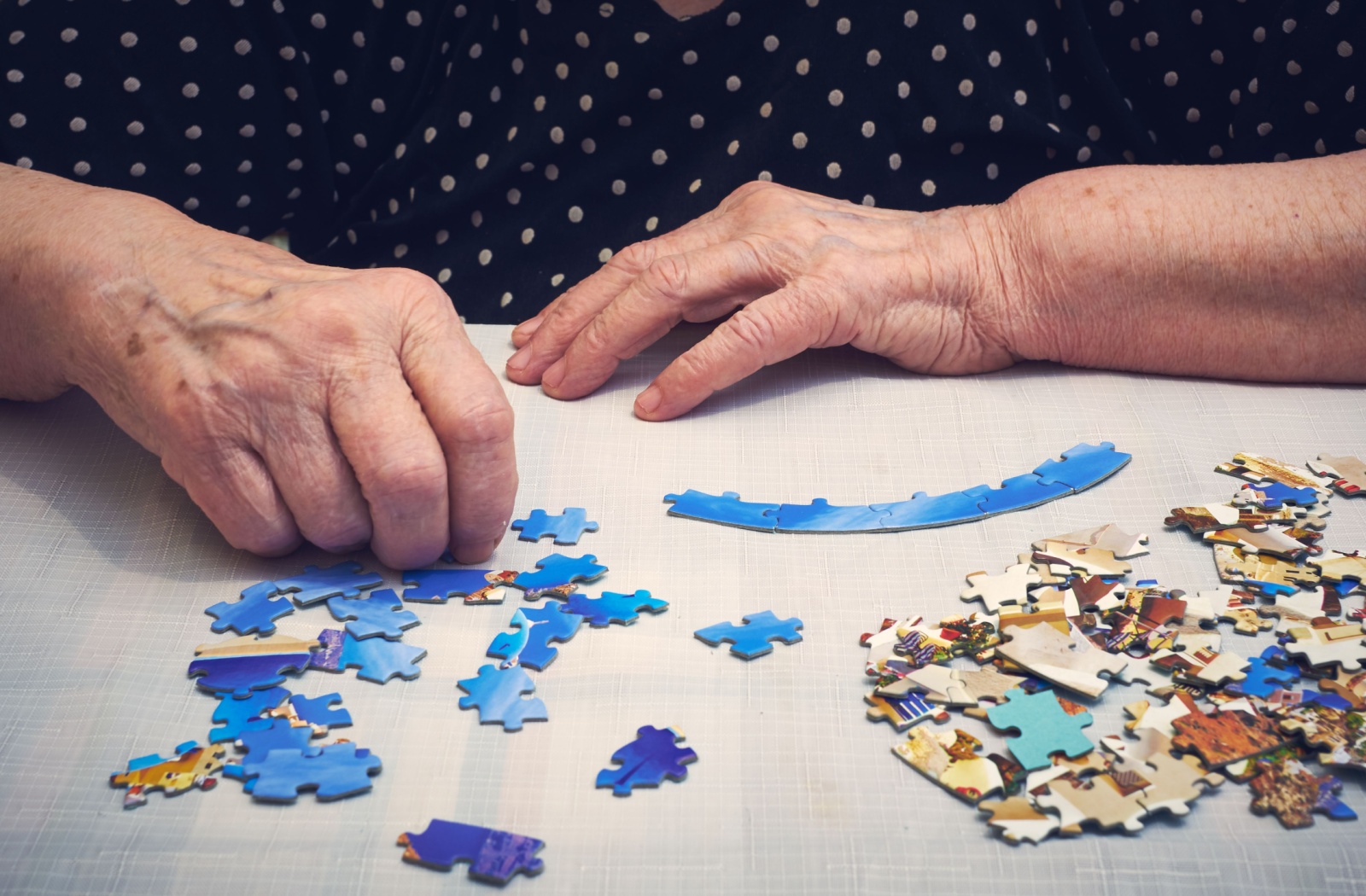 An elderly person working on a puzzle at a table