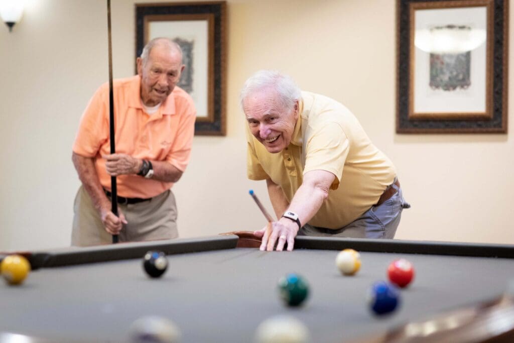 Two residents enjoying a game of pool indoors
